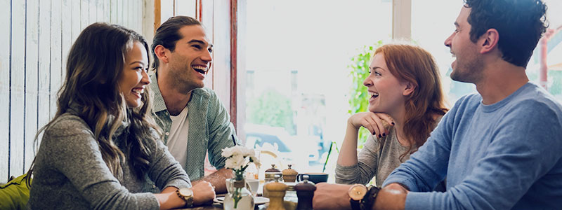 Image of two young couples at a cafe, captured in a moment of laughter and enjoyment, highlighting the warmth and connection shared among friends during a casual outing.