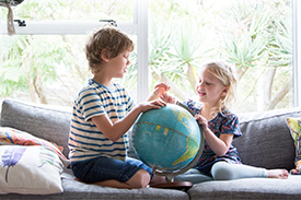 Young boy and girl sitting on a couch and looking at a globe of the world 