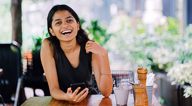 A smiling woman in a cafe while banking on her phone.