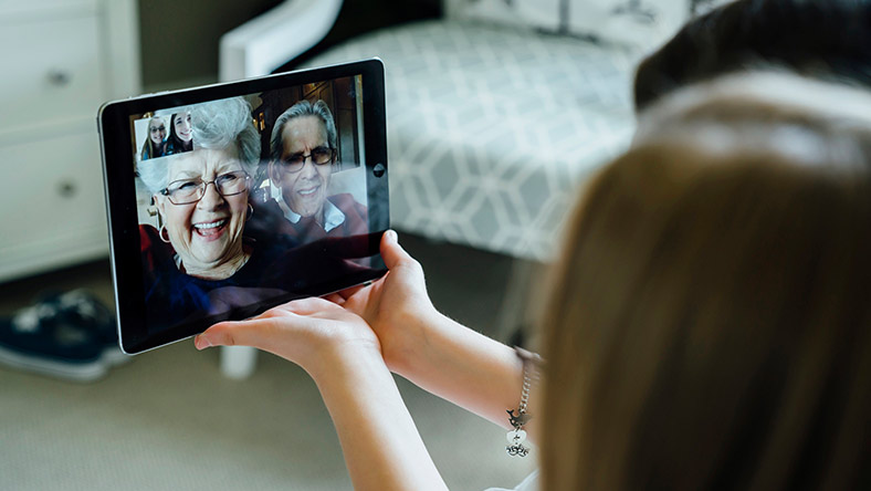 Two young women use a mobile tablet to enjoy a video call with their grandparents.