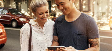 Happy couple look at phone smiling. The First Home Owners Deposit scheme gives eligible members the chance to own their first home sooner.