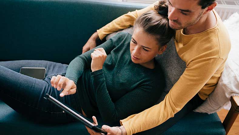 Man and woman sitting on sofa, looking at iPad