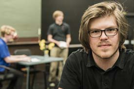 University student gazing to camera while lecturer talks to students in background