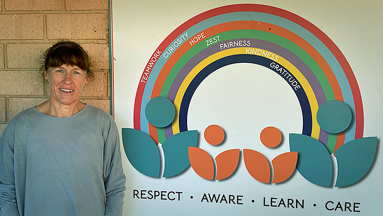 Alison Kerimofski stands in front of a sign with the words "Respect, Aware, Learn, Care" on it.