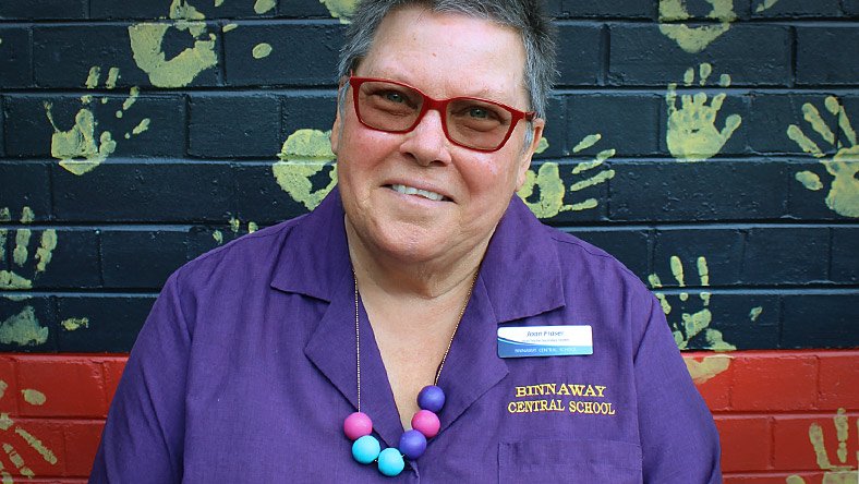 Joan Fraser of Binnaway Central School sits in front of a wall painted in the Aboriginal flag colours with handprints over it.