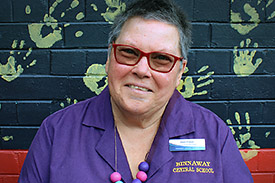 Joan Fraser of Binnaway Central School sits in front of a wall painted in the Aboriginal flag colours with handprints over it.