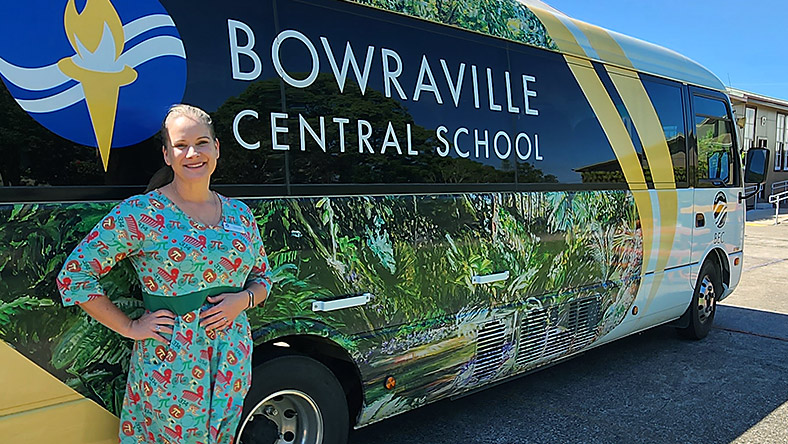 Marcia Bell stands in front of the Bowraville Central School bus. The bus is covered in decals of foliage.