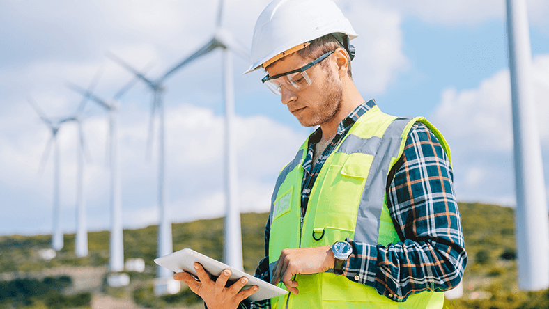 Man in hi-vis vest looking at iPad in wind farm