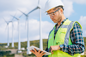 Man in hi-vis vest looking at iPad in wind farm