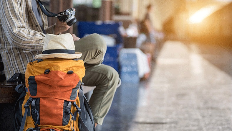 A man waiting at a train station with a large backpack and camera.