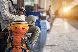 A man waiting at a train station with a large backpack and camera.