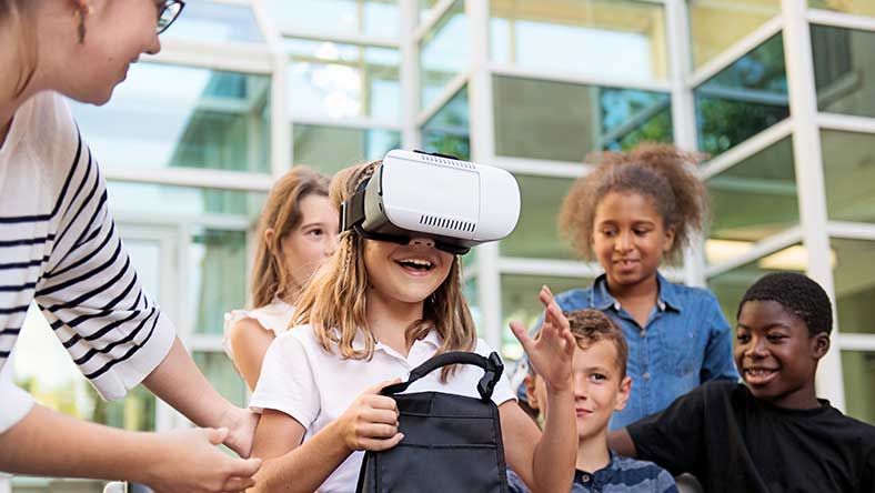 Excited group of children standing around little girl wearing goggles, while teacher assists