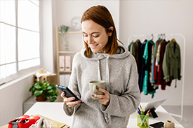 A woman looks at her phone in her right hand holding a mug in her other hand.