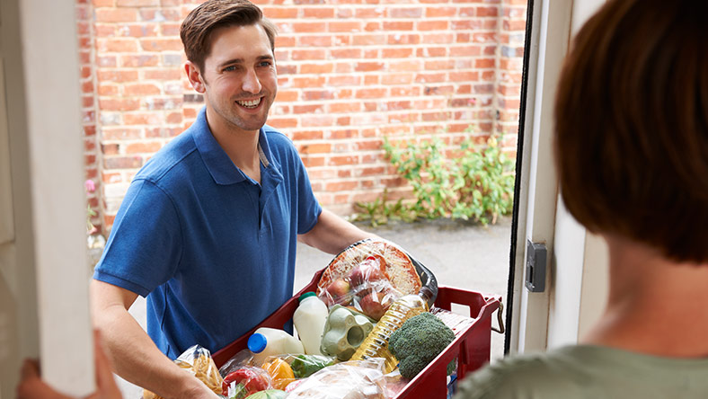 Man delivering box of fruit and vegetables to woman as part of food subscription service.