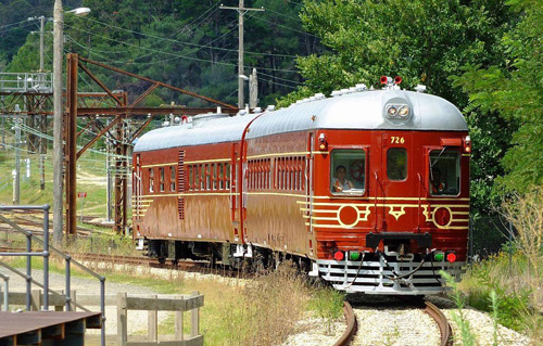 Red vintage diesel train with gold detail and chrome grills travelling down a country railway