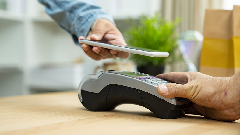 One hand uses a phone to pay for a purchase on an EFTPOS machine