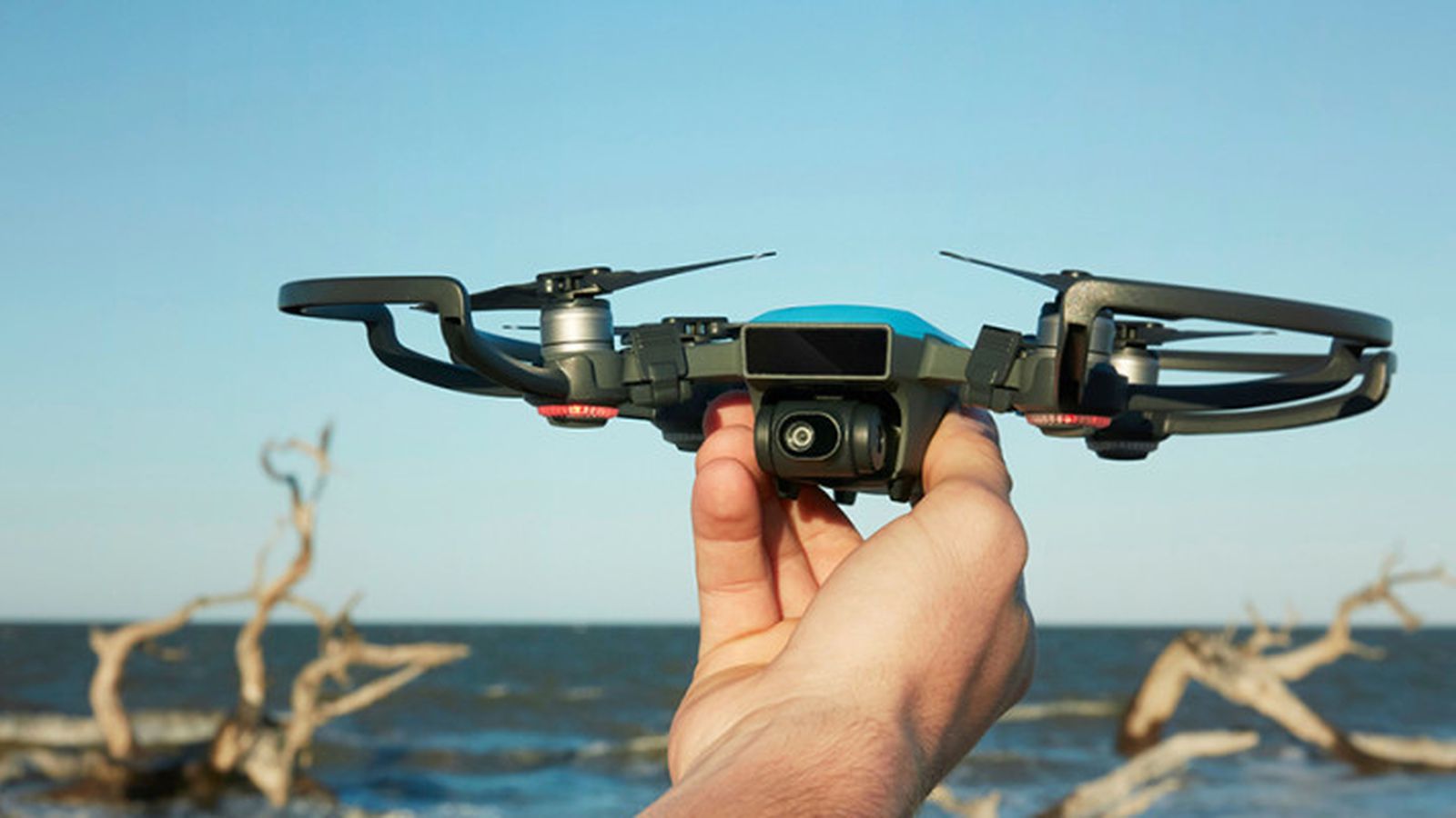 hand holding a small drone with a lake in the background