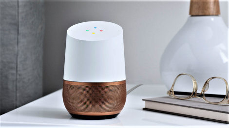 Google home sitting on a bedroom sidetable with lamp, book and glasses in view