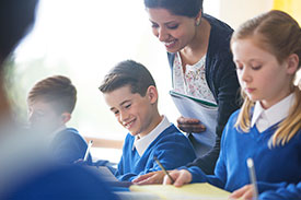 A female teacher in a classroom, smiling as she looks over a student's shoulder, symbolising Teachers Mutual Bank's support for educators and their commitment to positive learning environments.