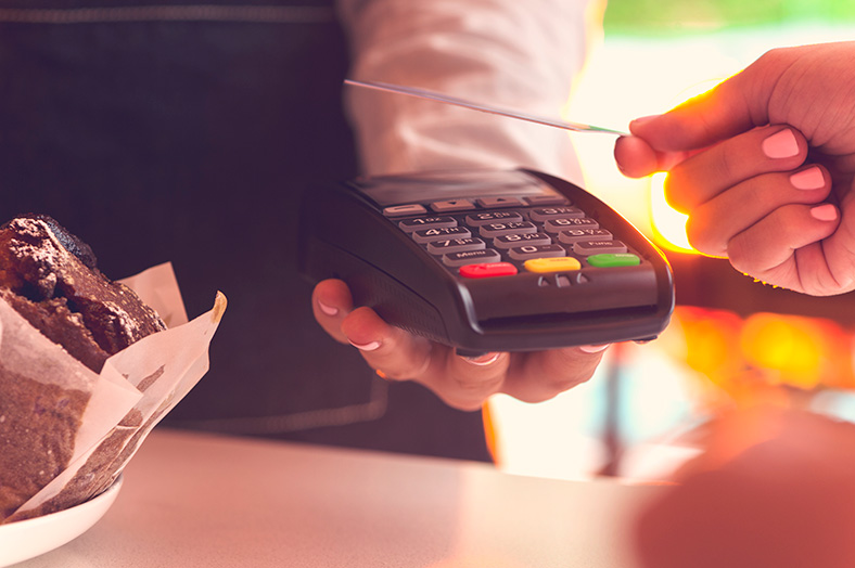 Person's hand ready to tap credit card on eftpos machine being held by business representative