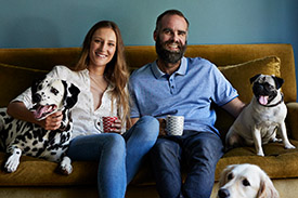 A happy couple sit on their lounge surrounded by pet dogs.