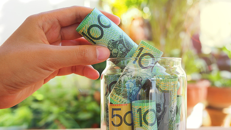 A hand places fifty and hundred dollar notes in an emergency fund jar.