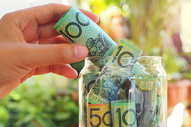 A hand places fifty and hundred dollar notes in an emergency fund jar.