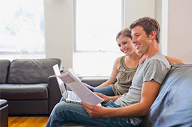 A couple sit on the couch in their home, reading documents to check their financial wellness.