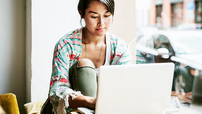 Young woman is on her laptop sitting by a cafe window.