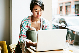 Young woman is on her laptop sitting by a cafe window.