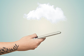 A person with a tattoo on forearm holds out a mobile phone while the foreground is made up of a single cloud and blue sky