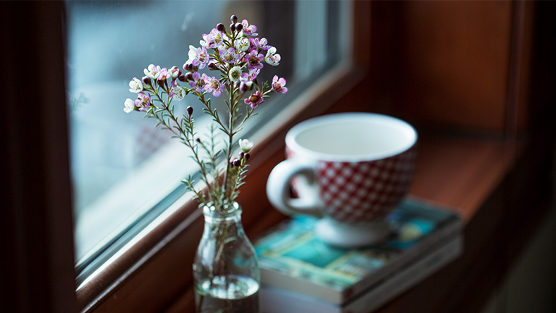 A vase of fresh spring flowers sits on a window sill next to a mug of tea.