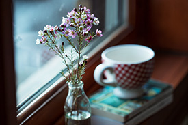 A vase of fresh spring flowers sits on a window sill next to a mug of tea.