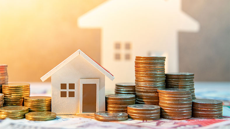 Toy block house surrounded by stacks of coins