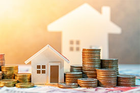 Toy block house surrounded by stacks of coins