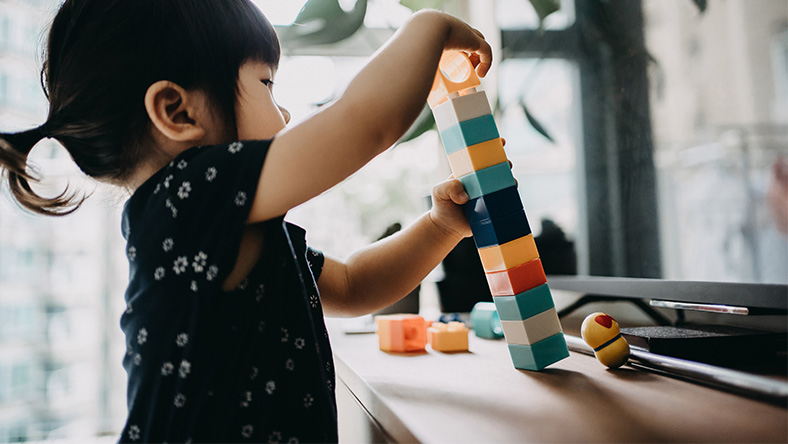 A young girl constructs a tower from coloured building blocks