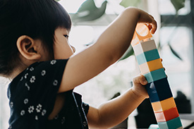 A young girl constructs a tower from coloured building blocks