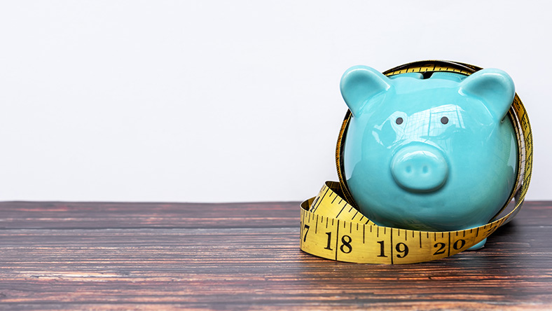 A tape measure is wrapped around a piggy bank.