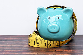 A tape measure is wrapped around a piggy bank.