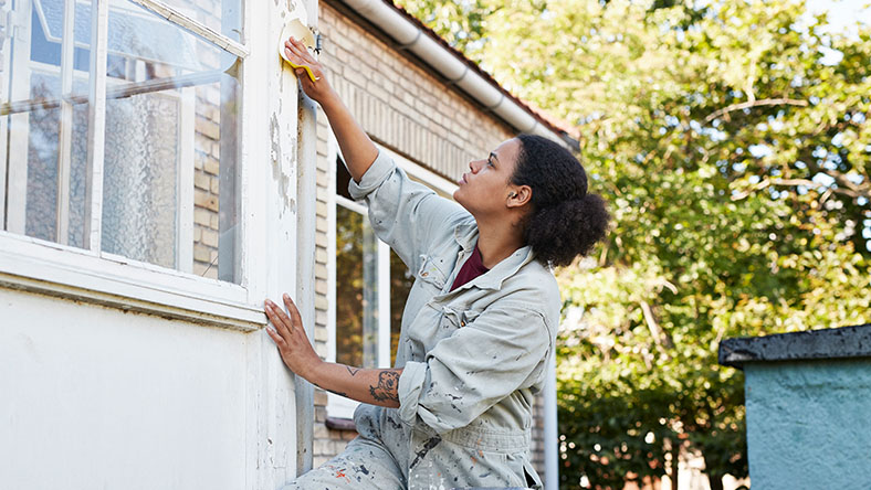 A young woman washes her windows from the outside of her house.