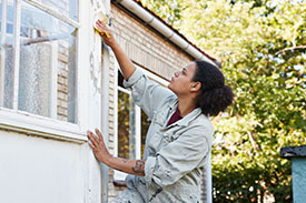 A young woman washes her windows from the outside of her house.