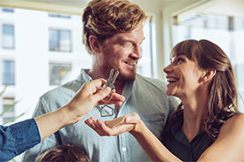 Man and woman looking at each other while being handed keys to new home