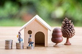 Small male and female figurines outside a miniature home made out of wood