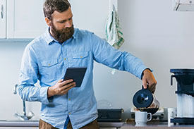 A man pours coffee from a pot into a cup in his kitchen.