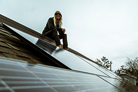 A young woman sits on a rooftop next to her solar panel grid observing the view.