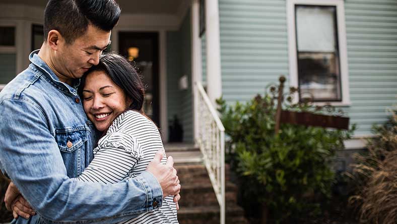 Young couple hugging in front of house