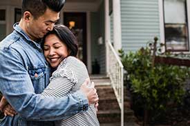 Young couple hugging in front of house