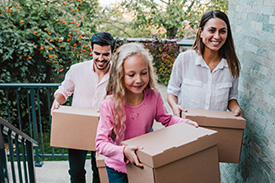 A young smiling family carry boxes into their new home.