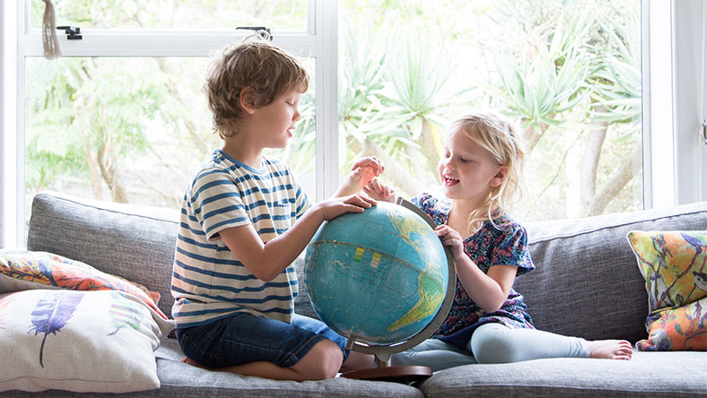 Young boy and girl sitting on a couch and looking at a globe of the world 
