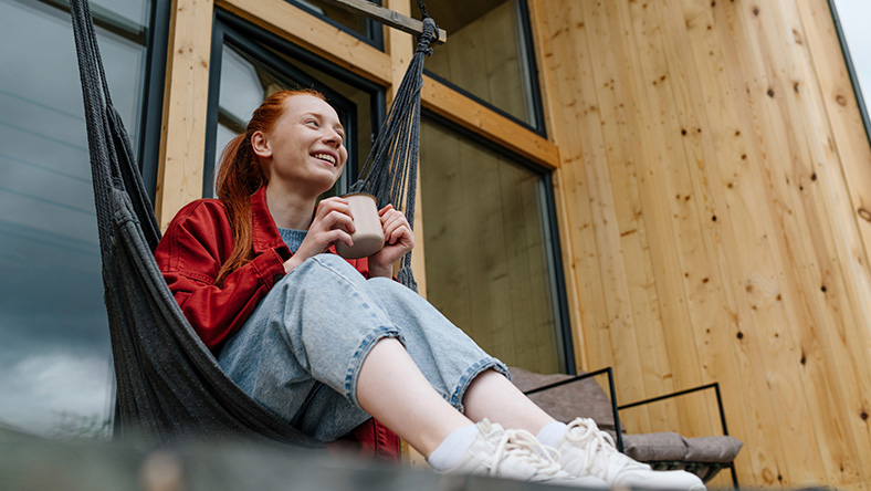 A woman sits in a hammock chair with a mug.